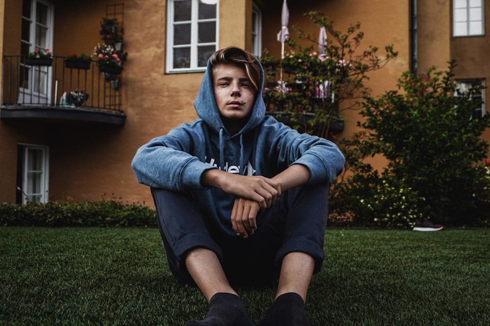 homme en veste à capuche bleue assis sur les herbes