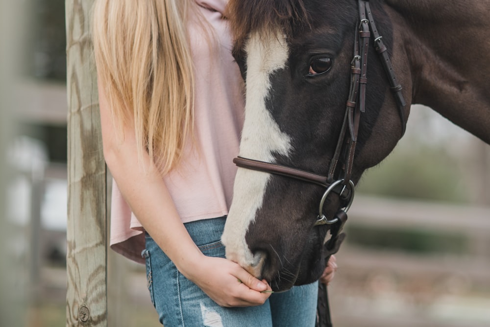 woman standing beside black and white horse at daytime