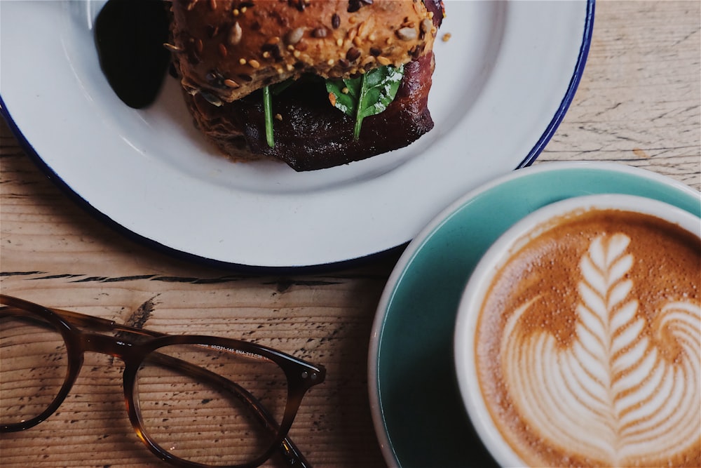 white ceramic cup filled with brown coffee beside eyeglasses