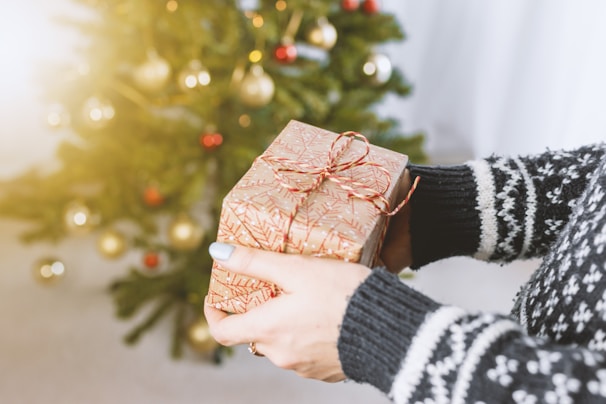 A close-up of Santa's hands holding a beautifully wrapped gift with a red ribbon, ready to be given during a home visit.