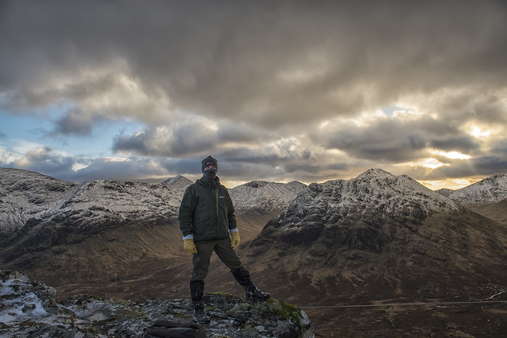 man standing on cliff overviewing rock mountain at daytime