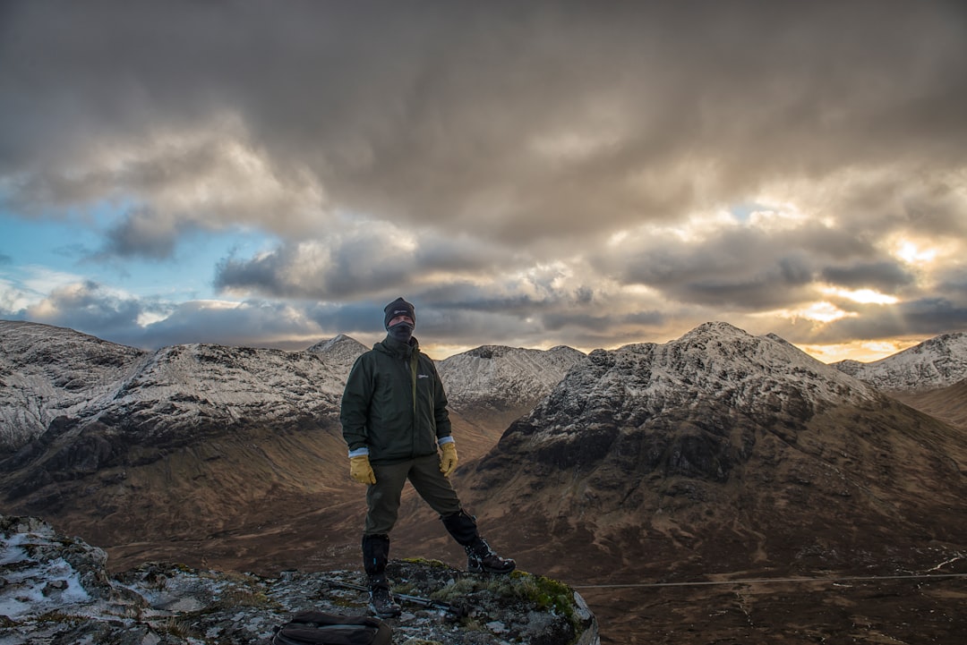 man standing on cliff overviewing rock mountain at daytime