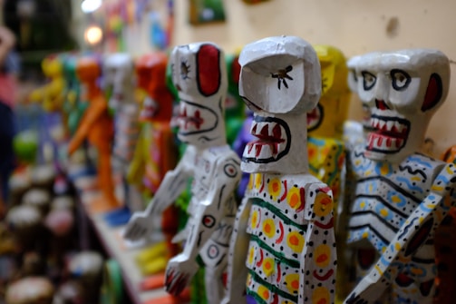 Hand-painted calavera figurines lined up on a shelf with warm lighting.