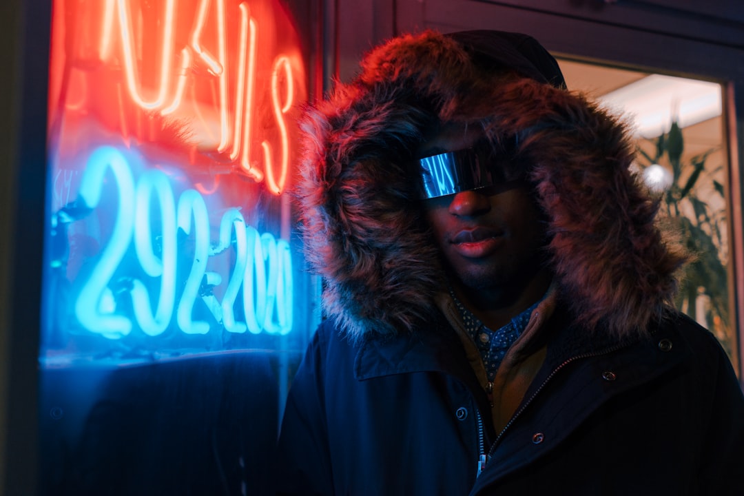 man in black full-zip hoodie leaning on neon light signage