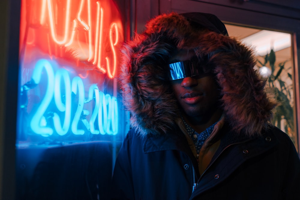 man in black full-zip hoodie leaning on neon light signage