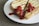Two slices of toasted cheese sandwich are placed on a white plate. The sandwich is topped with a generous amount of ketchup. The bread appears to be grill marked and crispy, and the filling consists of melted cheese.