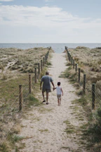 man and boy walking across pathway heading beach