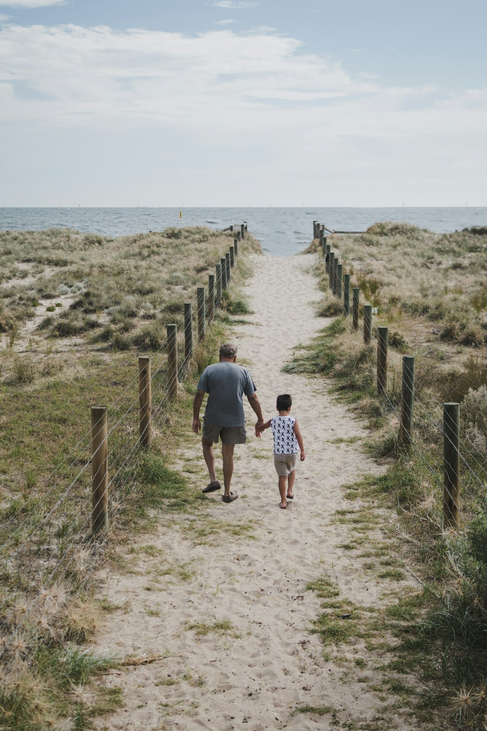 해변으로 향하는 통로를 가로질러 걷고 있는 남자와 소년