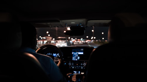 car interior from central back seat position showing driver and blurred view through windscreen of a busy road at night