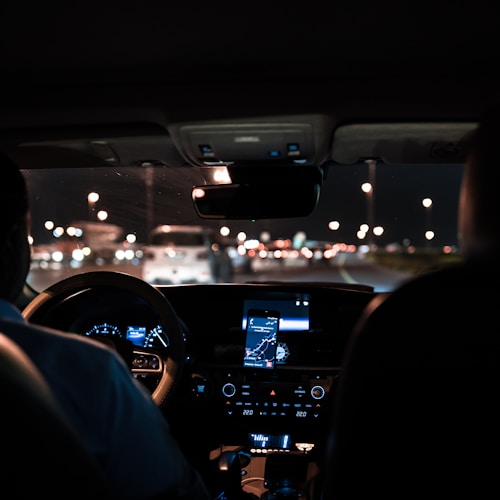 car interior from central back seat position showing driver and blurred view through windscreen of a busy road at night