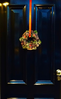 An elegant holiday wreath with rich greenery, red berries, and a satin bow hanging on a front door welcoming festive guests.