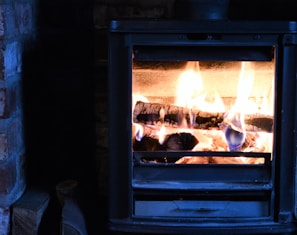 Poêle à bois en métal noir, avec des flammes vives et des bûches incandescentes à l'intérieur.