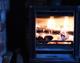 Poêle à bois en métal noir, avec des flammes vives et des bûches incandescentes à l'intérieur.