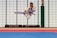 A martial artist performing a high kick in mid-air inside a dojo, wearing a white gi with a black belt. The background is a grid of translucent panels and training mats cover the floor.