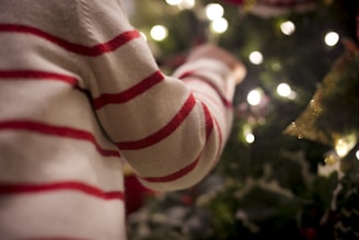 A happy child wearing a bright red Christmas sweater with reindeer patterns, smiling by a decorated Christmas tree.