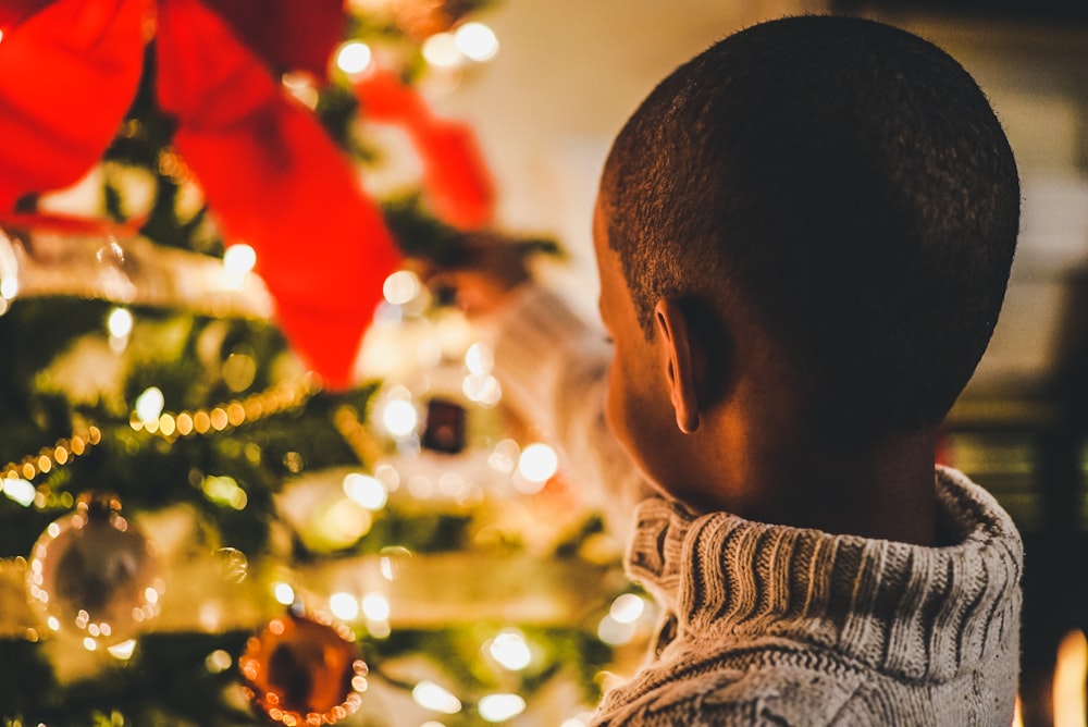 photographie sélective de mise au point d’un garçon près de l’arbre de Noël éclairé