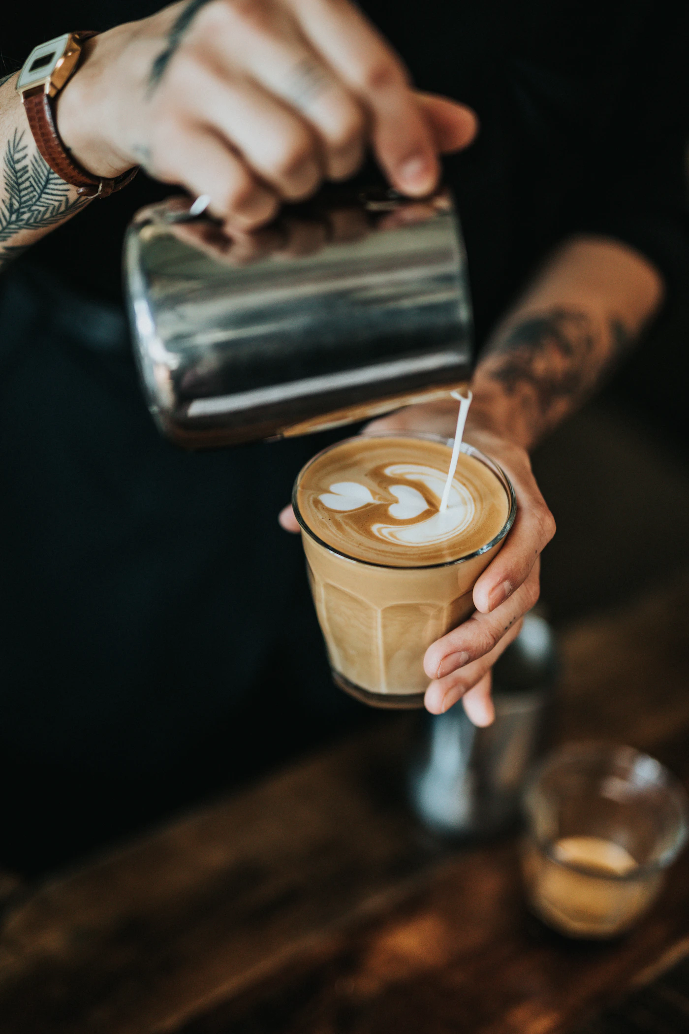 Barista pouring latte art into a glass of coffee
