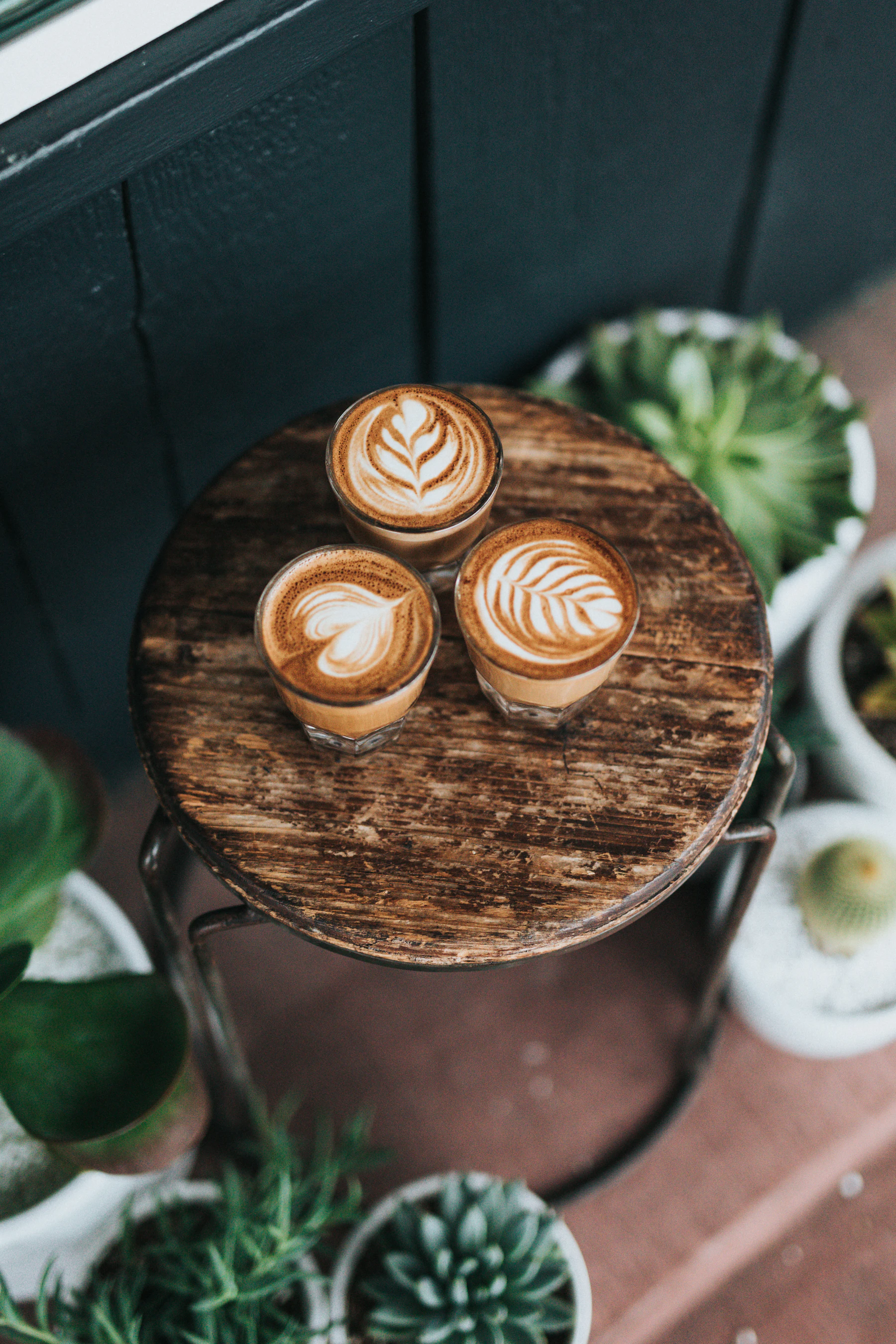 Three coffee cups on wooden stools inside a cozy independent coffee shop
