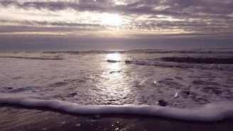 A vertical image of a calm beach at sunrise with gentle waves.