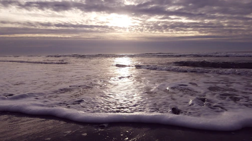 A vertical image of a calm beach at sunrise with gentle waves.