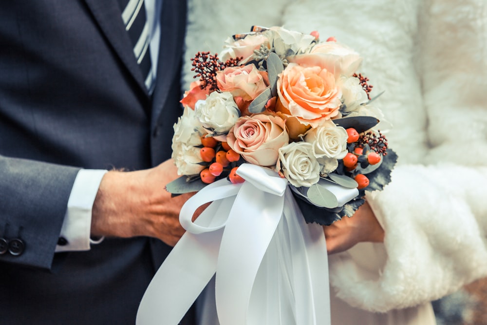 person holding orange and white flower arrangement