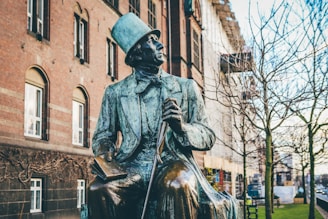 man in top hat and coat holding book and cane sitting statue
