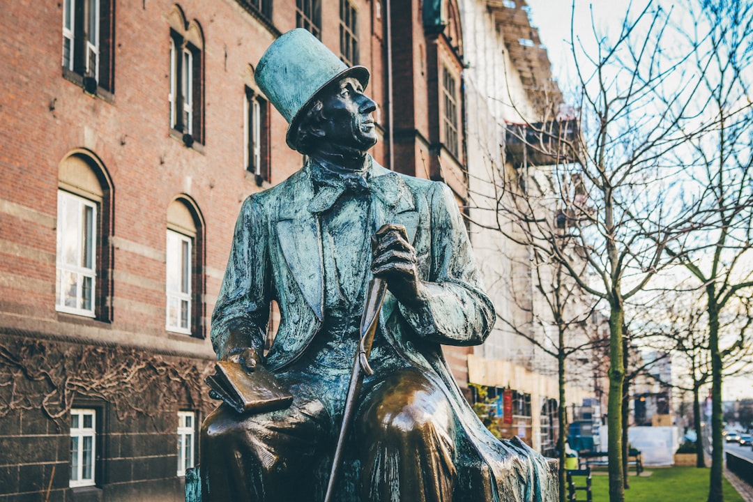 man in top hat and coat holding book and cane sitting statue