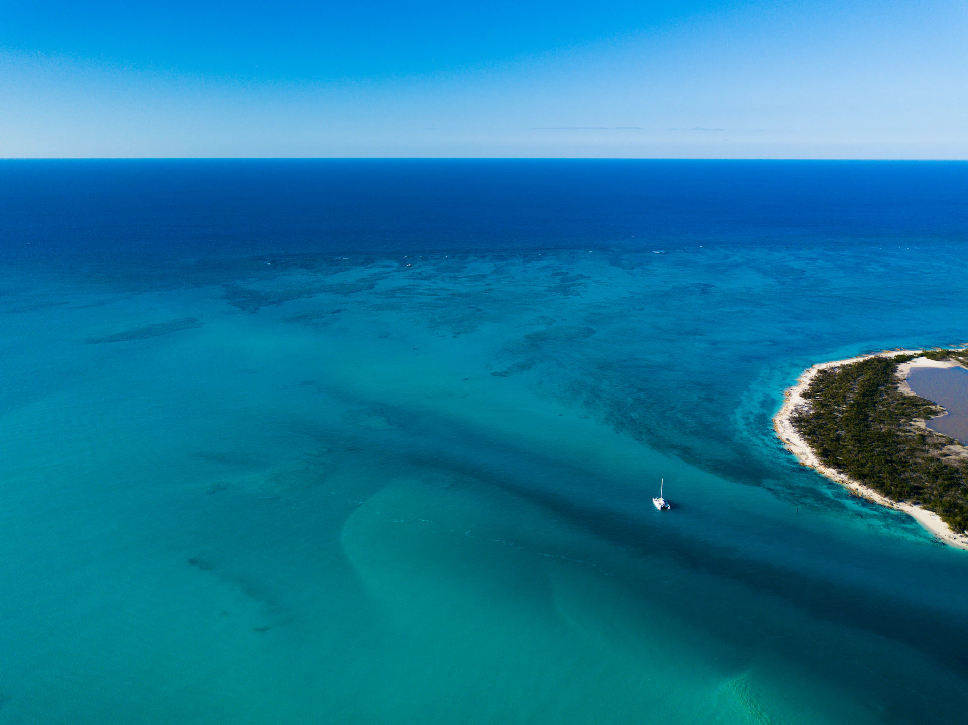 A crystal-clear turquoise ocean with a lone sailboat drifting near a tropical island.