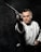 A person in a martial arts uniform is holding a katana sword with a focused expression, aiming it forward against a dark textured background. The scene conveys a sense of concentration and mastery in martial arts.