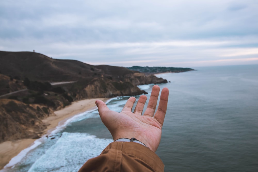 person hand front of sea and cliff