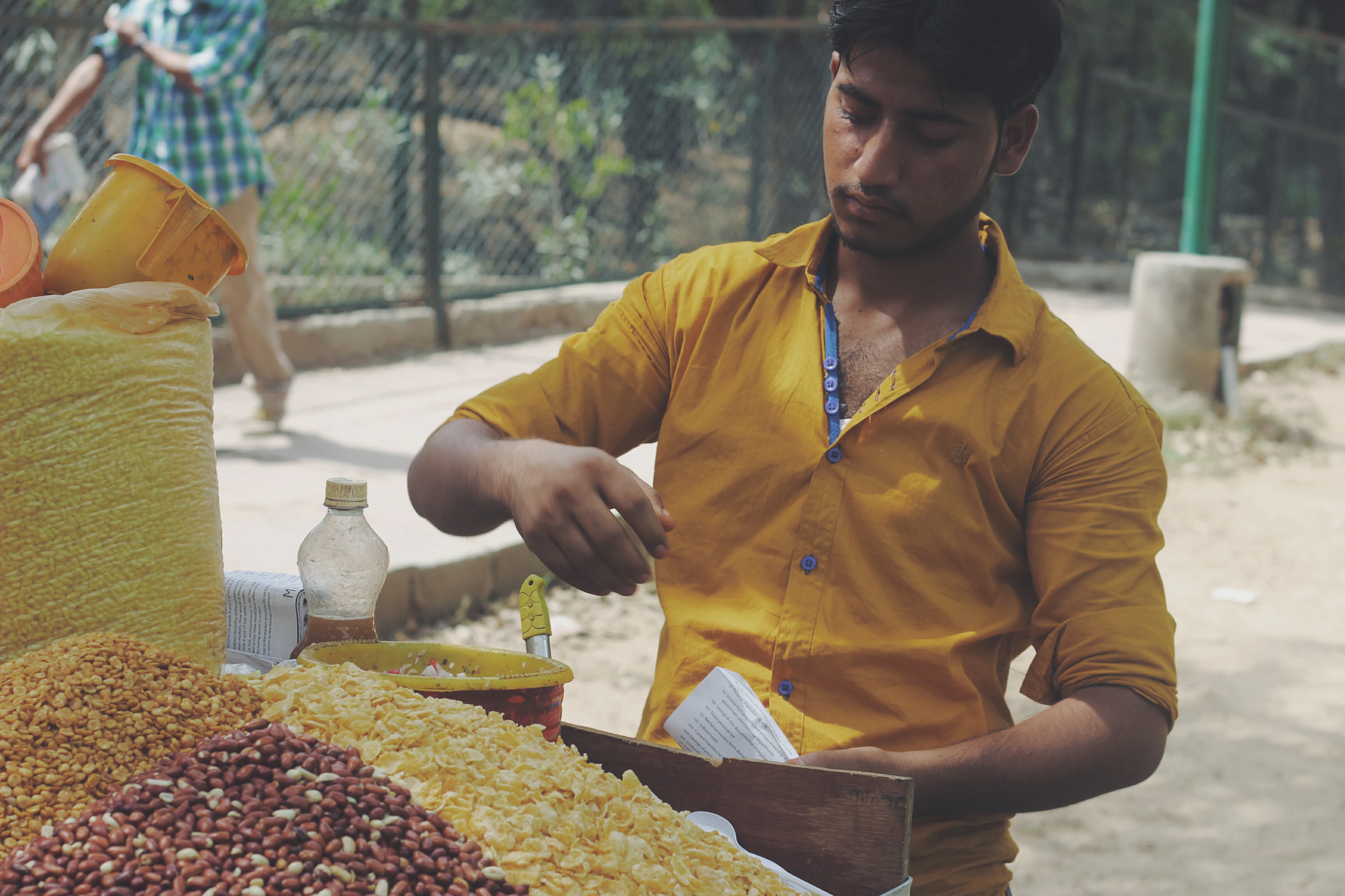 A street vendor in a yellow shirt mixes colorful lentils and snacks at an outdoor chaat stall.
