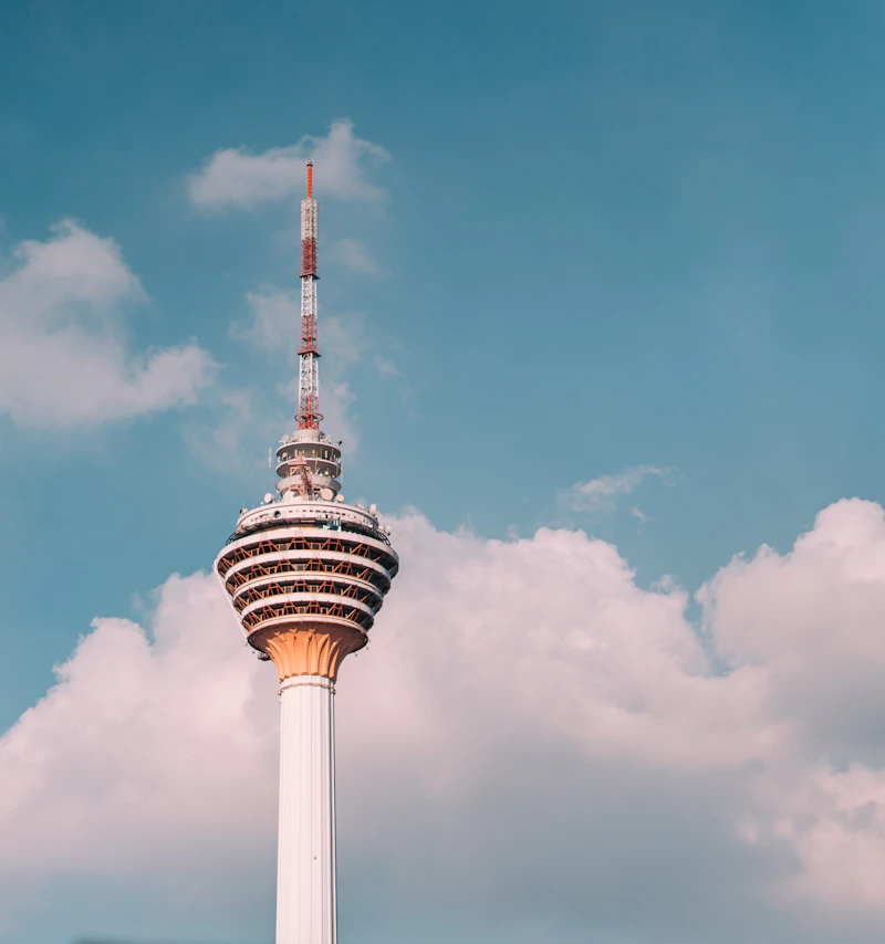 Close view of KL Tower against a blue sky with white clouds