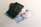 A green Indonesian passport is placed atop two banknotes of 50,000 Indonesian Rupiahs and two coins. The passport has a textured surface and the money is slightly visible beneath it.