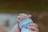 A close-up of an adult hand gently holding a baby's hand, conveying a sense of care and protection. The baby is wearing a white garment with a blue trim and colorful designs.