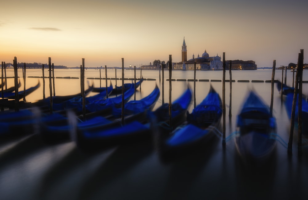 blue boats docking on calm body of water with castle in distance during sunrise