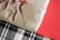 A gift wrapped in plain brown paper is tied with a red and white striped string. Attached is a brown paper tag with the text 'made in Santa's Workshop'. The background consists of a festive red color and a glimpse of a plaid pattern below the gift.