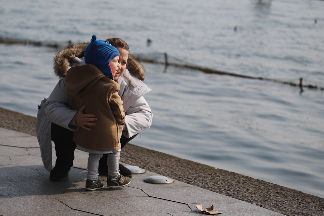 child standing on concrete bay together with sitting woman