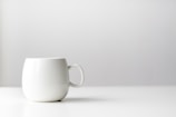 A close-up of a clean, white matte mug with a smooth finish against a soft grey background.