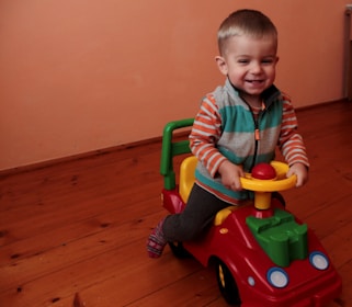 A pediatrician smiling while examining a happy child with colorful toys in the background.
