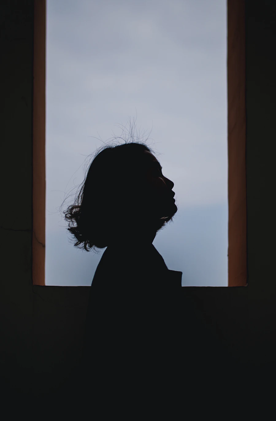 Silhouette de profil, visage levé, respiration calme devant une lumière bleu-gris
