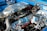 An intricately detailed car engine with polished metallic surfaces, including various tubes, hoses, and components. The engine is housed within a bright blue compartment and features shiny chrome finishes, suggesting high performance and customization.