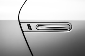 A close-up view of a car door focusing on the sleek, modern handle with a recessed design. The handle is embedded in the car's body, with a minimalist and streamlined appearance, showcasing a metallic finish.