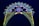 An illuminated arch constructed with numerous small lights forms a decorative pattern against a dark blue sky. The design includes floral and geometric shapes in green, blue, white, and yellow lights, with red flower-like bulbs scattered throughout.