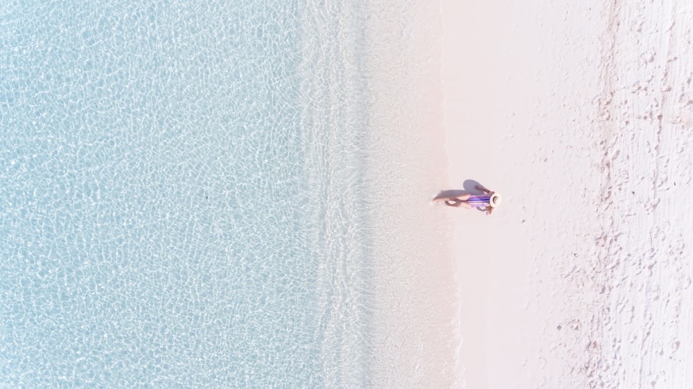 Luftaufnahme einer Person, die tagsüber auf dem Sand mit Blick auf das Meer sitzt