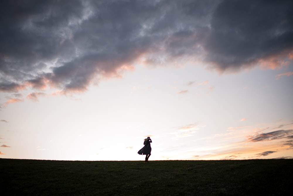 silhouette d’homme debout sur le sol sous ciel nuageux