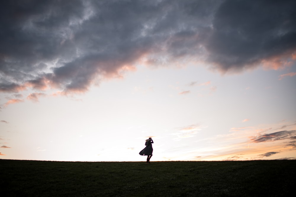 silhouette of man standing on ground under cloudy sky