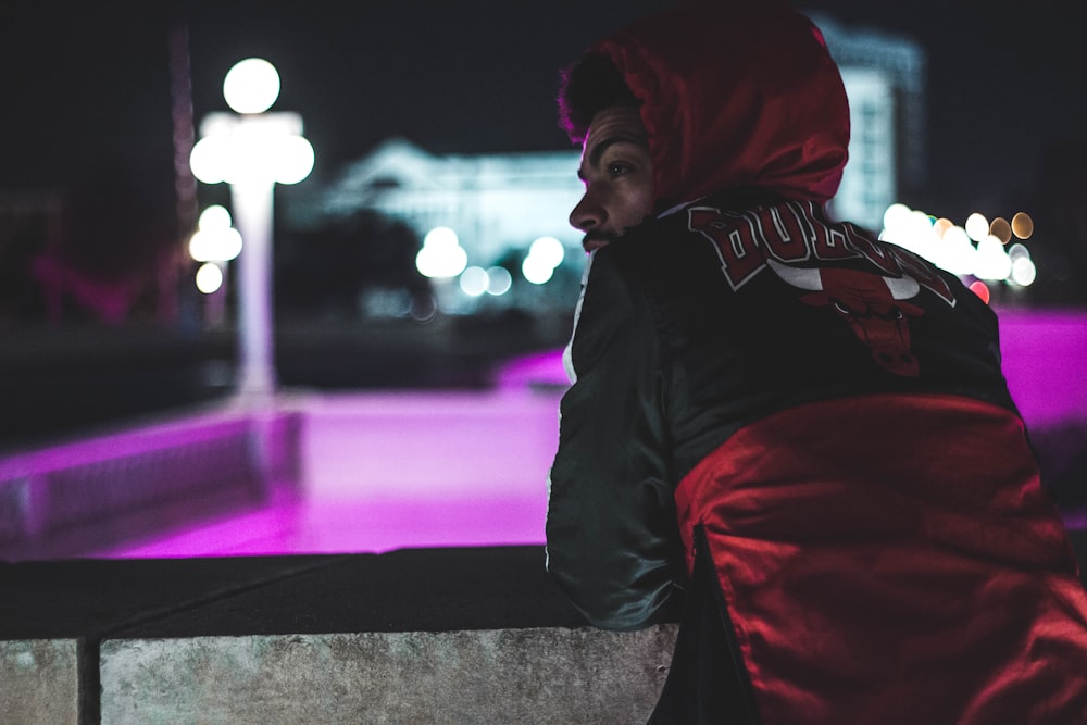 men wearing red and black hoodie leaning towards concrete barrier