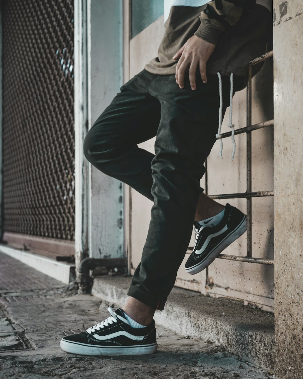 Un hombre apoyado contra una pared con zapatillas blancas y negras