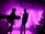 Silhouetted musicians perform on stage with a vibrant pink and purple backlight, creating an electric and energetic atmosphere. The figures of the band members and their instruments are visible against the illuminated backdrop.