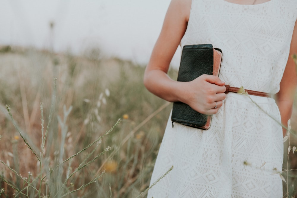 femme en robe blanche sans manches tenant un livre